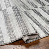 Close-up of the Gorou Taupe Area Rug showing a gray and white striped pattern and soft, textured pile on wood flooring. Fold