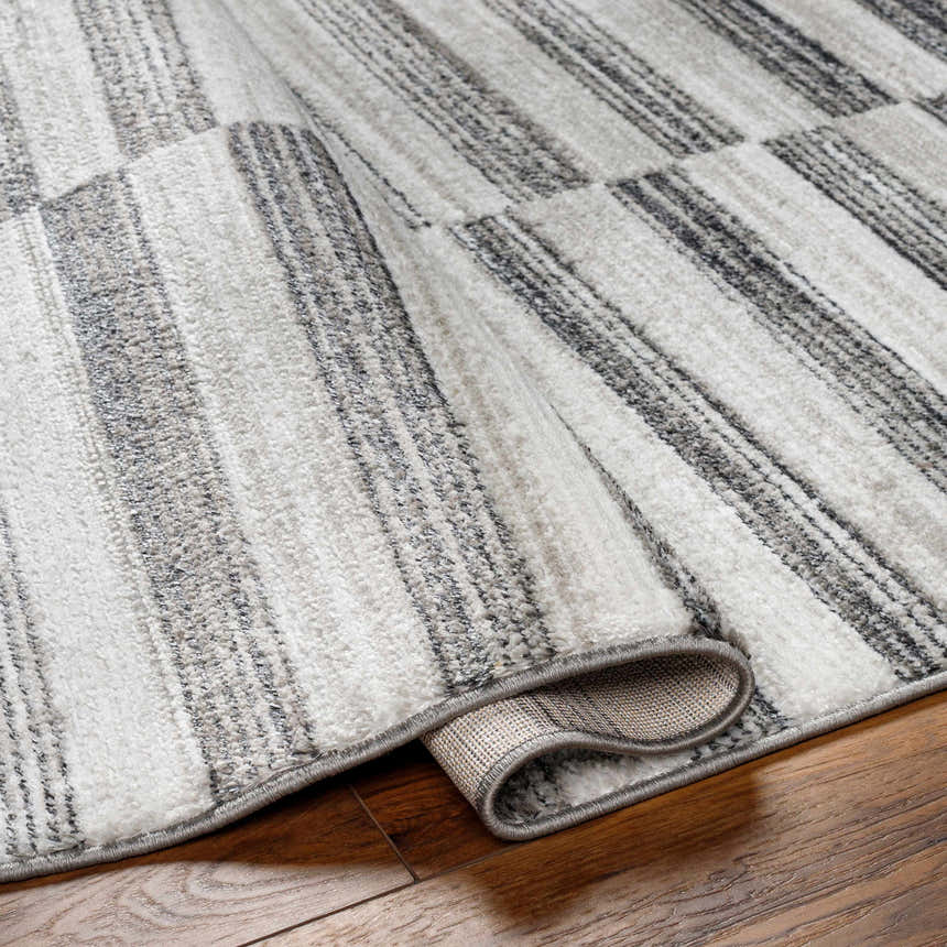 Close-up of the Gorou Taupe Area Rug showing a gray and white striped pattern and soft, textured pile on wood flooring. Fold