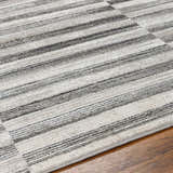 Close up of the Gorou Taupe Area Rug showing a striped design with shades of gray and ivory on hardwood flooring. Texture
