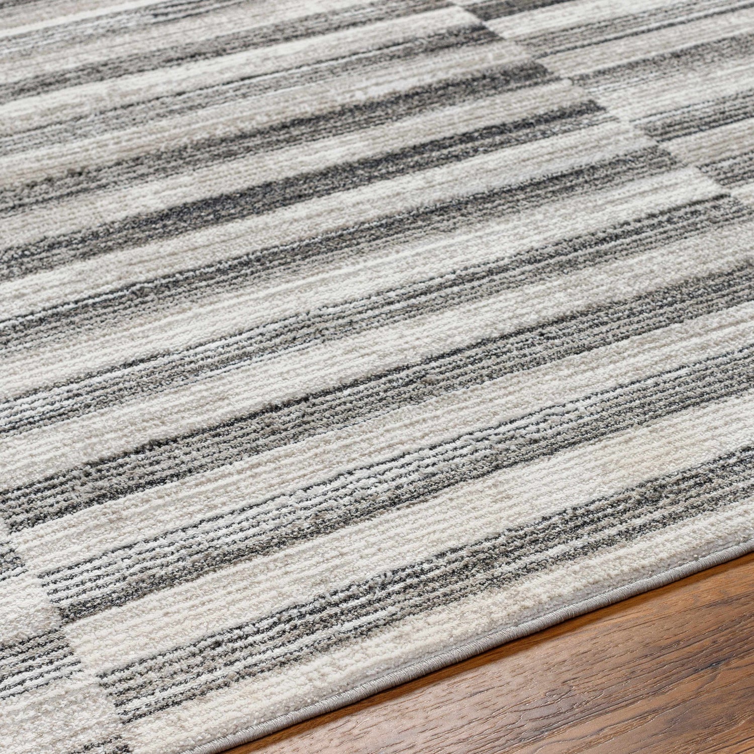Close up of the Gorou Taupe Area Rug showing a striped design with shades of gray and ivory on hardwood flooring. Texture