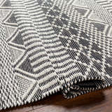 Close-up of the hand woven Carly Area Rug. Dark gray and off white geometric design. Contemporary, Scandinavian style. Fold