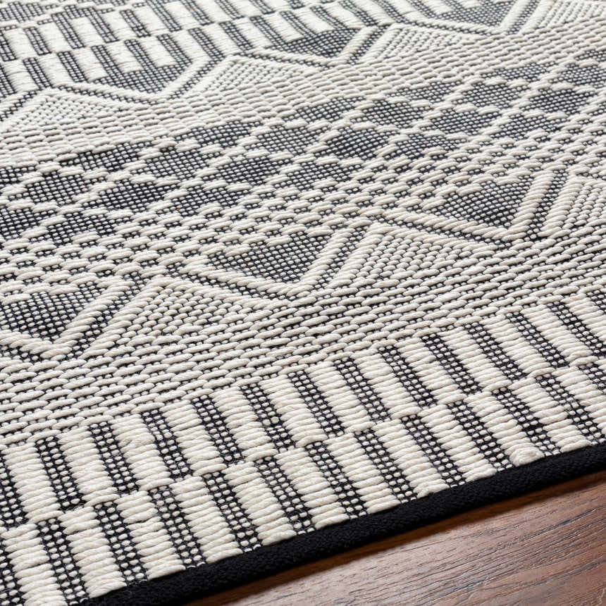 Close up of the Carly Area Rug, a hand woven wool rug with a geometric design in dark gray and off white. Texture