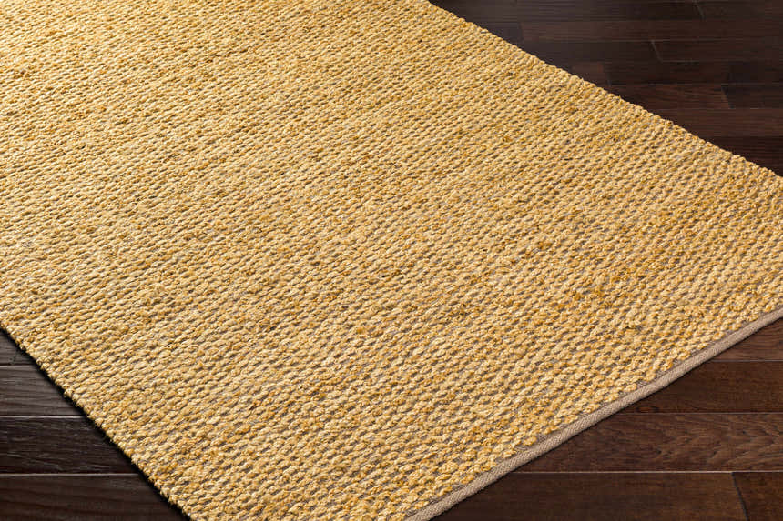 Close-up of Doris Beige Area Rug showing hand woven jute and cotton texture and neutral camel color on dark wood floor. Corner