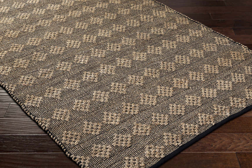 Close-up of the hand-woven Irina Area Rug. Medium brown and nutmeg jute and cotton rug with a geometric pattern. Corner
