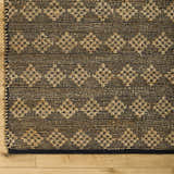 Close-up of the hand woven Irina Area Rug. Medium brown and nutmeg jute and cotton rug with geometric pattern. Corner