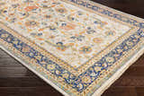 Close-up of the hand-knotted Starford Carpet. Farmhouse style rug with a floral pattern in ivory, blue, and orange on dark wood floors. Corner