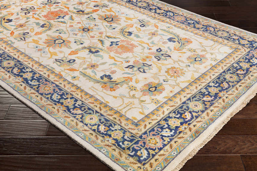 Close-up of the hand-knotted Starford Carpet. Farmhouse style rug with a floral pattern in ivory, blue, and orange on dark wood floors. Corner