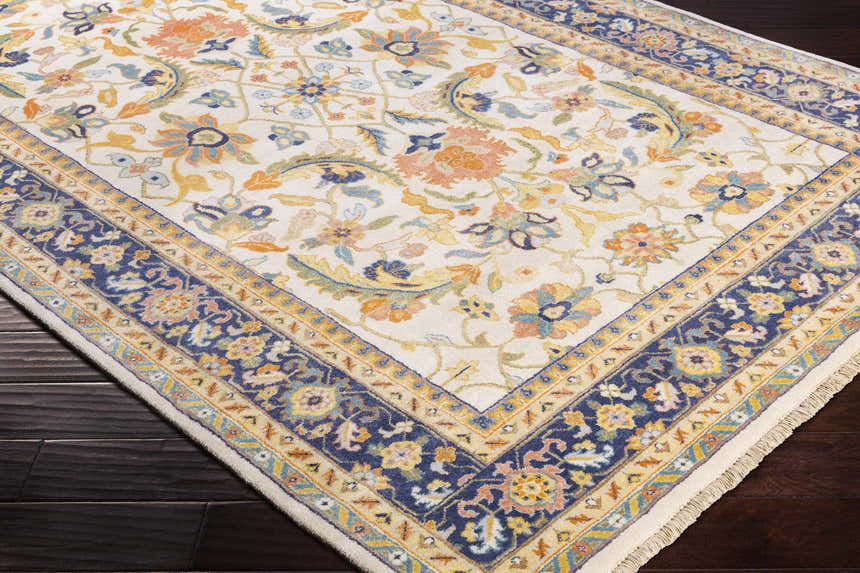 Close up of the hand knotted Starford Carpet. Farmhouse style rug with floral pattern in cream, blue, and orange. Corner
