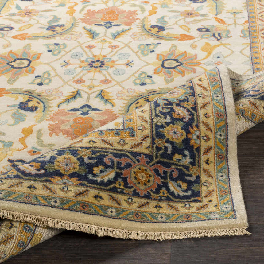 Close-up of the hand-knotted Starford Carpet. Farmhouse style rug with floral pattern in cream, blue, peach, and gold tones. Fold