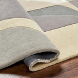 Close-up of the hand-tufted Duru Area Rug, featuring a geometric pattern in beige and gray tones. 70% wool texture. Fold