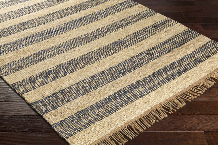 Close-up of Stapleford Striped Jute Carpet. Cream, navy, and tan stripes with jute fringe on dark wood floor. Corner
