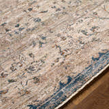 Close-up of the Stratmoor Area Rug showing beige, blue, and burnt orange traditional pattern on wood floor. Texture