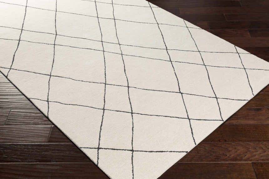 Close-up of the Strathalbyn Area Rug, a cream wool rug with a black geometric grid pattern on dark wood floors. Corner