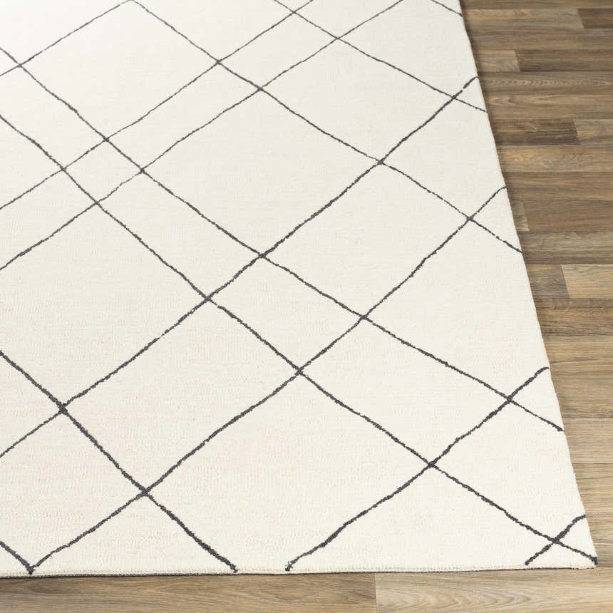 Close-up of the Strathalbyn Area Rug. Cream wool rug with a black geometric diamond pattern on a wood floor. Front