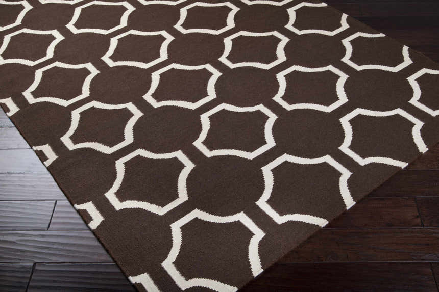 Close-up of the Sulligent Area Carpet rug. Features a brown background with a white geometric pattern. Hand woven wool texture. Corner