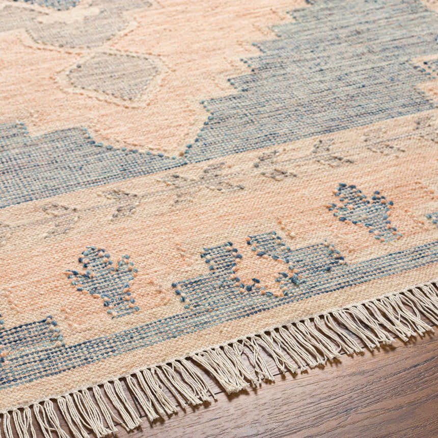 Close up of the hand woven Lana Area Rug showing its peach and blue traditional pattern and fringe. Texture