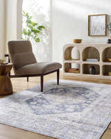 Living room scene with a blue and beige Keola Washable Area Rug, gray chair, and arched display cabinet. Roomscene-Rectangle