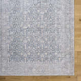 Close-up of the Odele Washable Area Rug. Medium gray, farmhouse style, traditional floral pattern on wood floor. Corner