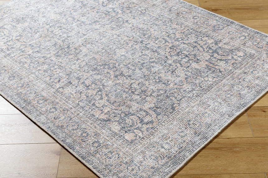 Close-up of the Orsin Washable Area Rug, a traditional rug with a gray, cream, and blush floral pattern on wood floors. Corner