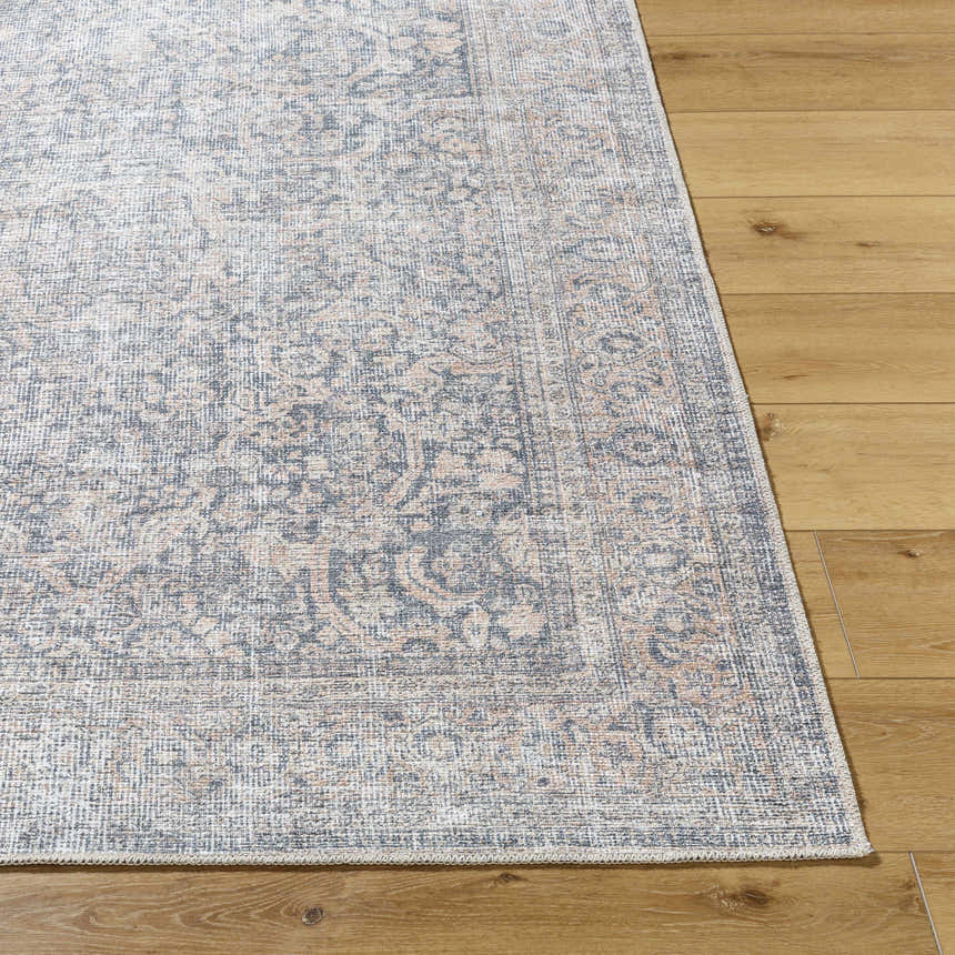 Close-up of the Orsin Washable Area Rug, a traditional rug with gray, peach, and white tones on a wood floor. Front