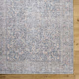 Close up of the Orsin Washable Area Rug showing traditional pattern in blue, peach, and cream on a light wood floor. Corner