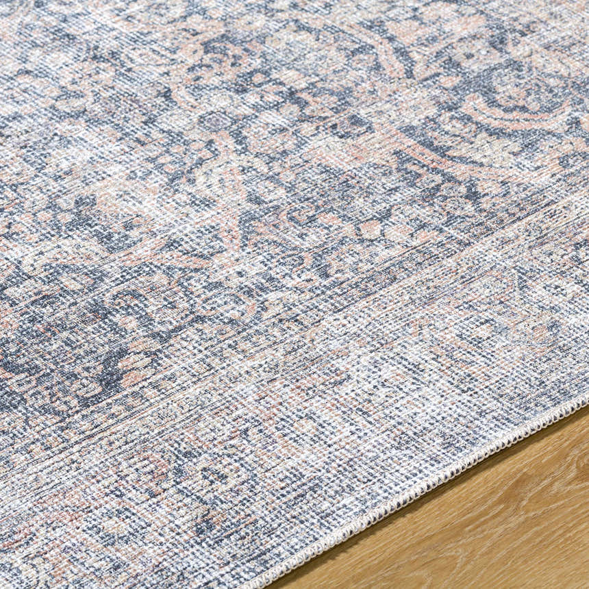 Close-up of the Orsin Washable Area Rug. Traditional style rug with a detailed pattern in gray, peach, and white tones. Texture