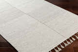 Close-up of the hand woven Abhay Beige Wool Area Rug showing its texture, geometric pattern, and tassels on dark wood flooring. Corner