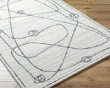 Close-up of the Sabah Area Rug. Light silver and off-white rug with a contemporary, abstract line and circle design. Hand-tufted texture. Corner