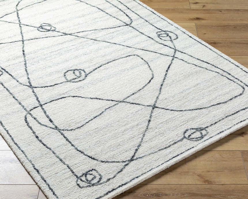 Close-up of the Sabah Area Rug. Light silver and off-white rug with a contemporary, abstract line and circle design. Hand-tufted texture. Corner
