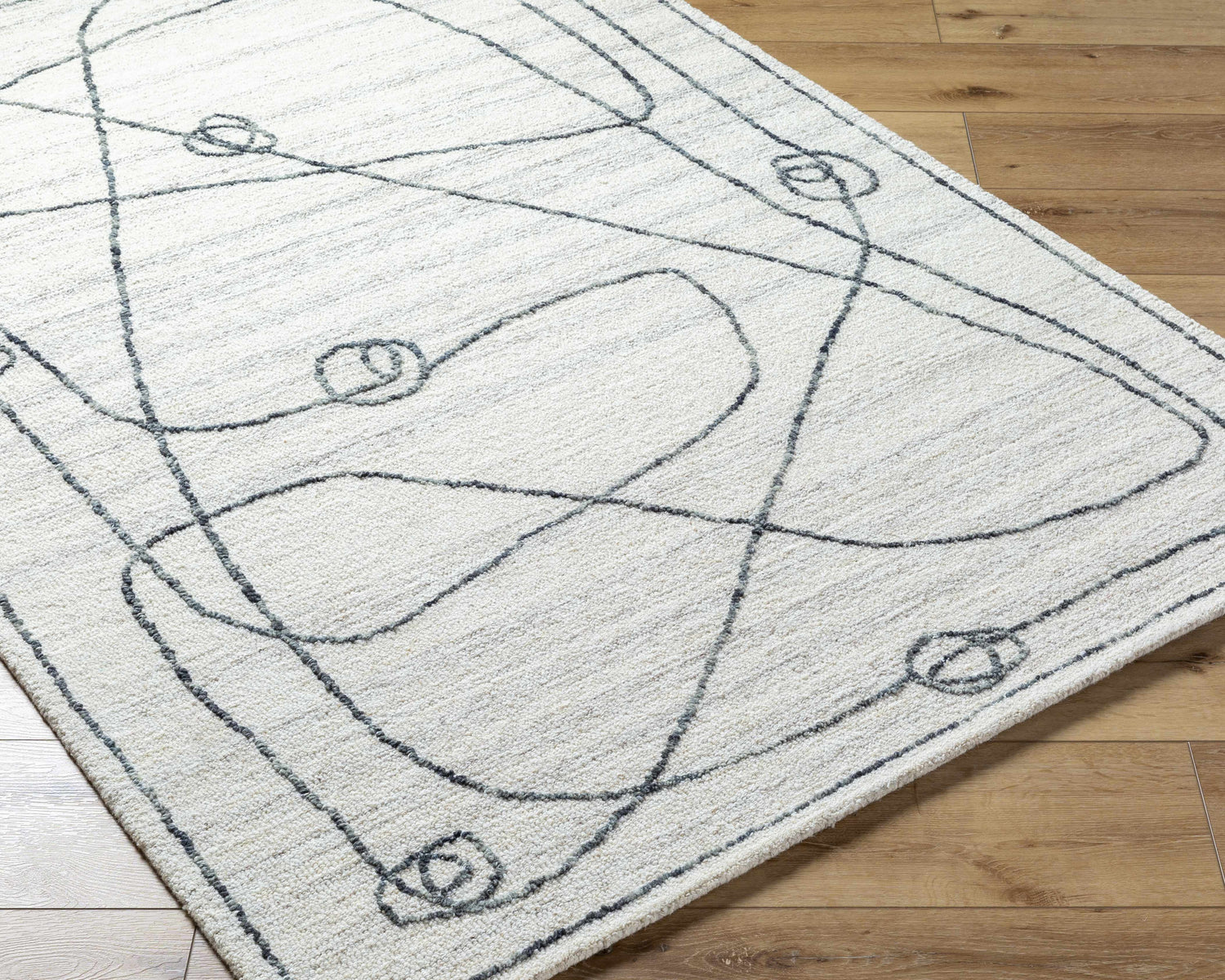 Close-up of the Sabah Area Rug. Light silver and off-white rug with a contemporary, abstract line and circle design. Hand-tufted texture. Corner
