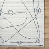 Close-up of the Sabah Area Rug, a hand-tufted rug with a light silver and off-white abstract design. Corner