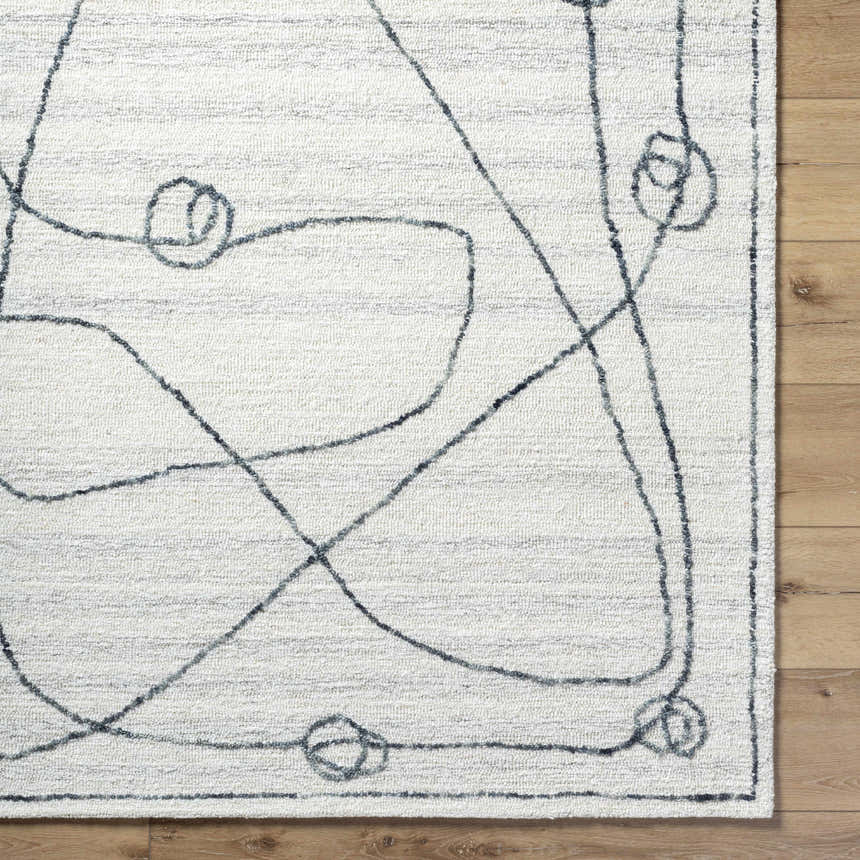 Close-up of the Sabah Area Rug, a hand-tufted rug with a light silver and off-white abstract design. Corner