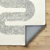 Close-up of the Saura Wool Area Rug showing its ivory color and charcoal dotted, curved line design. Fold