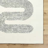 Close-up of the Saura Wool Area Rug. Ivory rug with a contemporary charcoal dotted line pattern on a wood floor. Corner