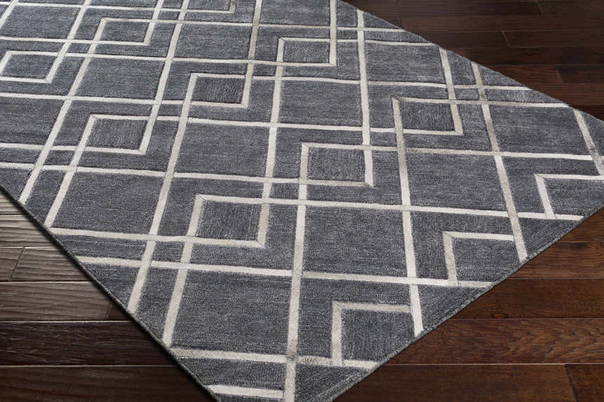 Close-up of the Taclobo Area Rug showing a gray viscose rug with a geometric light gray pattern on dark wood floors. Corner