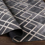 Close-up of the Taclobo Area Rug, a gray rug with a geometric pattern and a hand-crafted construction. Fold