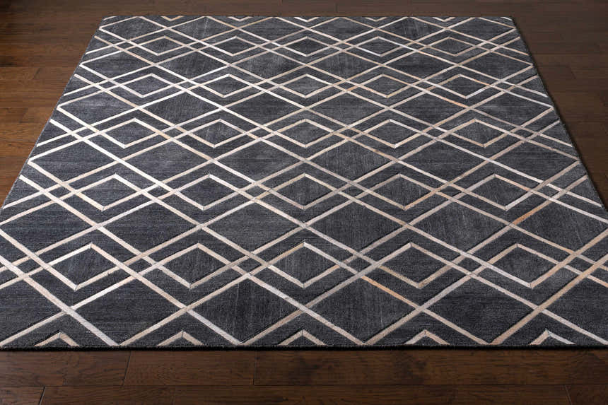 Close-up of the Taclobo Area Rug on dark wood floor. Black rug with light gray geometric diamond pattern. Front
