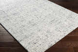 Close-up of the hand-tufted Tanana Area Rug. Cream wool rug with a subtle black and gray contemporary design. Corner