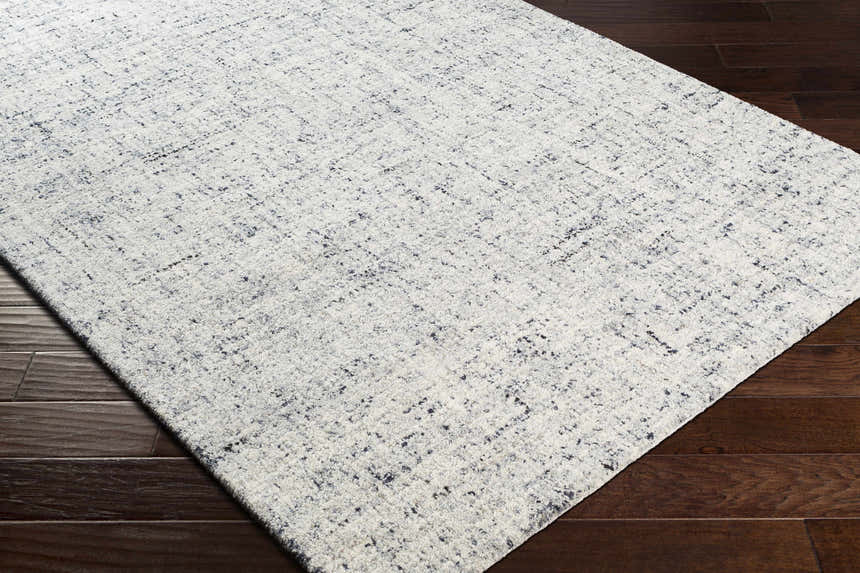 Close-up of the hand-tufted Tanana Area Rug. Cream wool rug with a subtle black and gray contemporary design. Corner