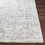 Close-up of the hand-tufted Tanana Area Rug showing its cream base with black and gray flecks on a wood floor. Front