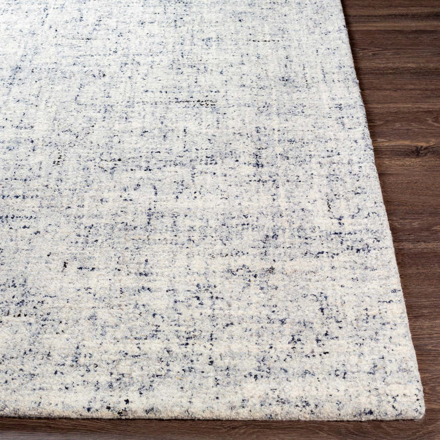 Close-up of the hand-tufted Tanana Area Rug showing its cream base with black and gray flecks on a wood floor. Front