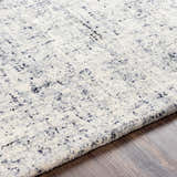 Close-up of the Tanana Area Rug, a hand-tufted wool rug in cream, gray, and black on a wood floor. Contemporary style. Texture