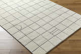 Close-up of Tanya Pearl White Grid Wool Rug on wood floor. Off-white rug with a contemporary square grid pattern. Corner