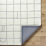 Close-up of the Tanya Pearl White Grid Wool Rug showing its off-white color, grid pattern, and hand-tufted texture. Fold