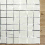 Close-up of the Tanya Pearl White Grid Wool Rug. Hand-tufted, off-white wool with a gray grid pattern. Contemporary style. Corner