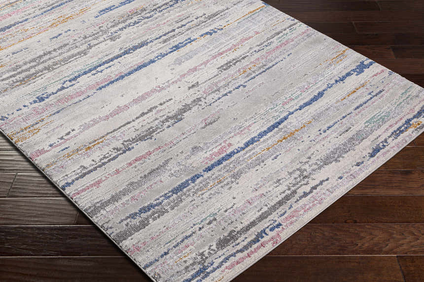 Close-up of the Tekirova Striped Area Carpet. Contemporary design with stripes in blue, pink, gold, and gray on a light background. Corner