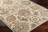 Close-up of the hand-tufted Teom Area Rug. Beige wool rug with a traditional floral pattern in camel, brown, and teal tones. Corner