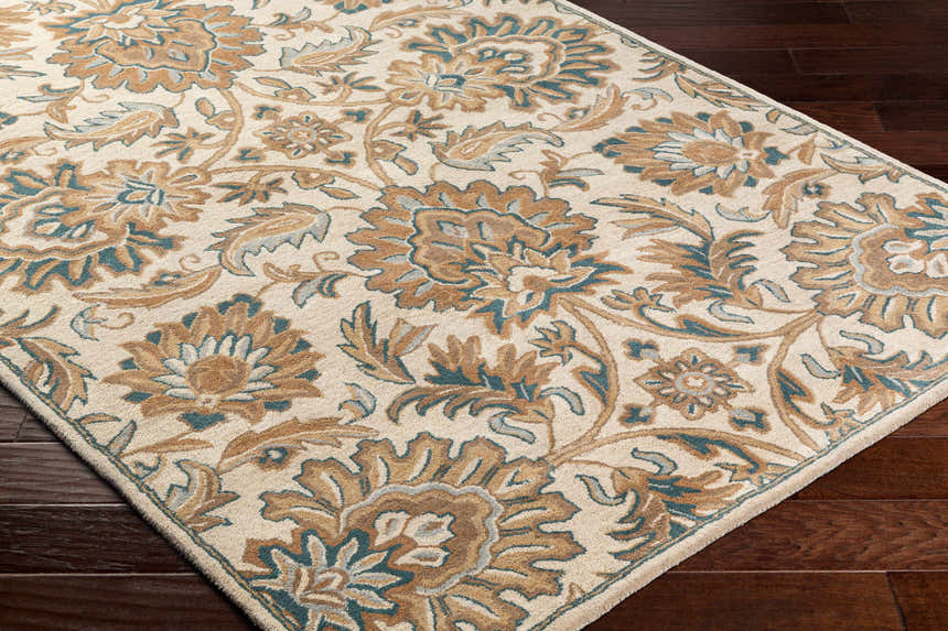 Close-up of the hand-tufted Teom Area Rug. Beige wool rug with a traditional floral pattern in camel, brown, and teal tones. Corner