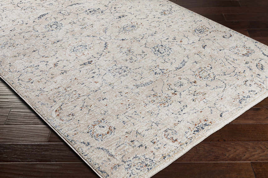 Close-up of the Ternate Area Rug showing its cream, denim, and brick red traditional pattern on dark wood floors. Corner