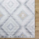 Close-up of the Tyipa Area Rug. Southwestern style rug in charcoal, cream, gray, and mustard on a wood floor. Corner